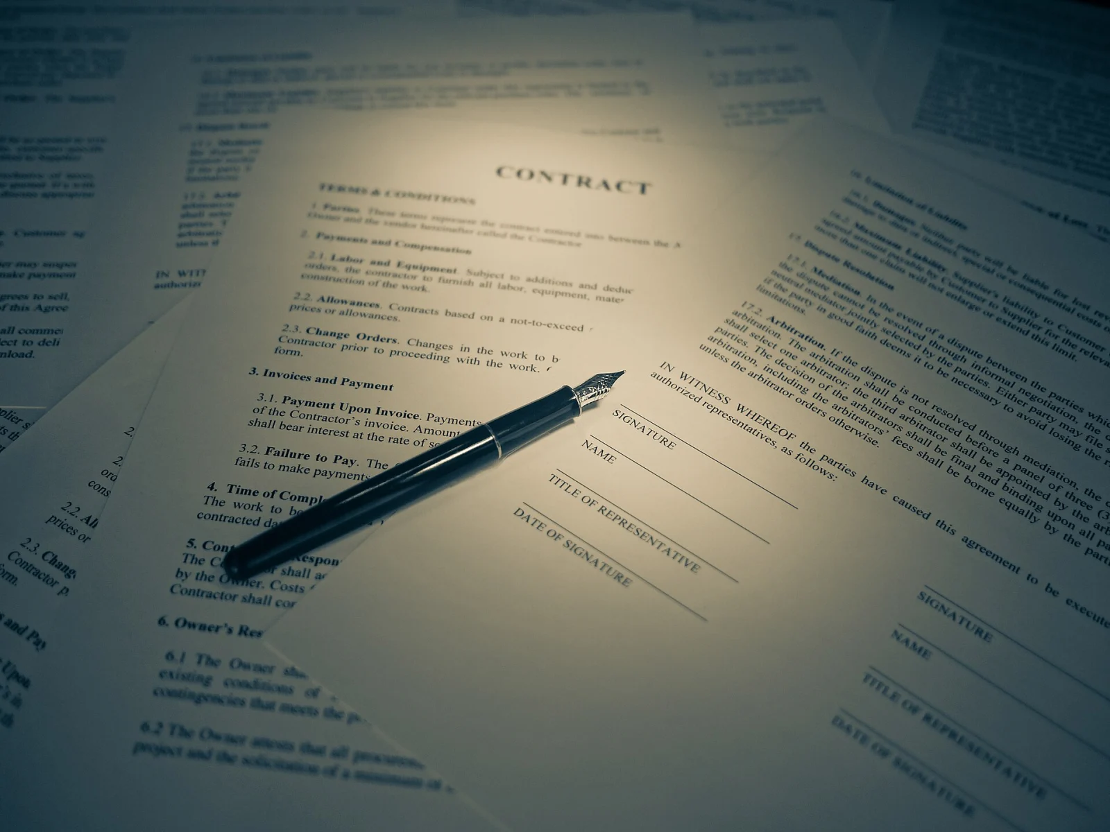 Un stylo noir pos&eacute; sur des documents contractuels, photographi&eacute;s en gros plan dans des tons chauds.